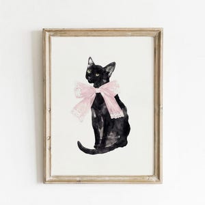 May include: A black cat with green eyes wearing a pink bow with lace trim. The cat is sitting on a white background.