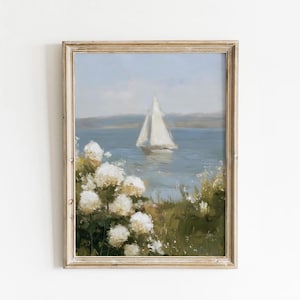 May include: A framed painting depicts a sailboat on a blue lake under a light blue sky. White flowers and green foliage are in the foreground. The frame is a light, neutral color.