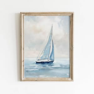 May include: A framed painting of a sailboat on the water. The artwork features a light blue sailboat with a white sail, set against a backdrop of a cloudy sky and blue water. The frame is a light, neutral color.