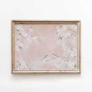 May include: A rectangular framed wall art piece featuring a soft, muted pink background with painted white cherry blossom branches extending from the corners. Two small, light-colored birds are perched on a central branch in the middle.