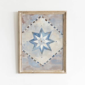 May include: A framed wall art print featuring a central eight-pointed star in shades of blue and white. The star is set within a diamond-shaped border of blue and white squares, all against a soft, muted, and cloudy beige and gray background.