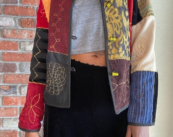 May include: A colorful patchwork jacket with embroidered details and yellow buttons. The jacket is made of different fabrics and textures, including velvet, corduroy, and cotton.