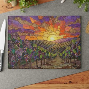May include: Rectangular cutting board with a stained glass design of a vineyard at sunset. The image features rows of grape vines, a path leading to the sun, and a colorful sky with shades of purple, orange, and gold.