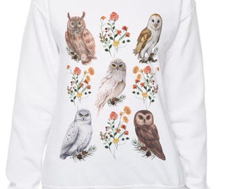 May include: White sweatshirt with a colorful print of owls and flowers. The owls are in various poses and colors, including brown, white, and gray. The flowers are pink, orange, and yellow.