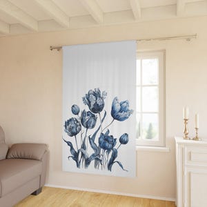 May include: A white curtain featuring a watercolor illustration of blue tulips. The floral design includes detailed petals and green stems. The curtain hangs in front of a window, with a glimpse of the outside visible.