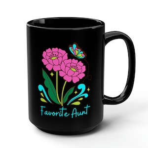 Könnte beinhalten: Schwarze Keramik-Kaffeetasse mit einem Blumendesign und dem Text "Favorite Aunt" in Blau. Das Design zeigt rosa Blumen, grüne Blätter und einen blauen Schmetterling.