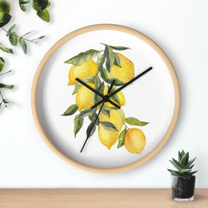 May include: A round wall clock with a light wood frame. The clock face features a watercolor painting of lemons and green leaves. Black clock hands indicate the time. The clock is on a wooden surface.