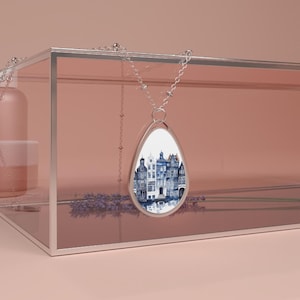 May include: A silver necklace with a teardrop-shaped pendant featuring a watercolour illustration of a row of blue and white houses reflected in a canal.