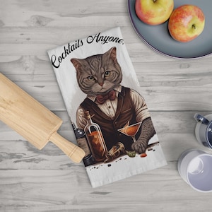 May include: A gray and white cat wearing a tuxedo and bow tie is holding a glass of cocktail. The cat is standing behind a bar with a bottle of liquor and a shaker. The text "Cocktails Anyone." is printed on the white background.