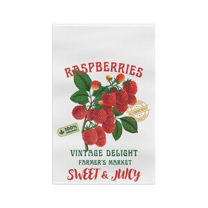 May include: White kitchen towel with a vibrant illustration of ripe red raspberries on a green leafy branch. The towel features text that reads "Raspberries," "Vintage Delight," "Farmer's Market," and "Sweet & Juicy."