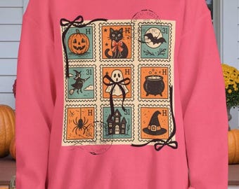 Può includere: Felpa rosa con un collage di francobolli a tema Halloween. I francobolli raffigurano una zucca, un gatto nero, una strega, un fantasma, un ragno, una casa infestata, un calderone e un cappello da strega. I francobolli sono arancioni, verde acqua e neri.