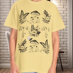 May include: A yellow t-shirt with a black and white graphic print of mushrooms, butterflies, bees, and flowers.