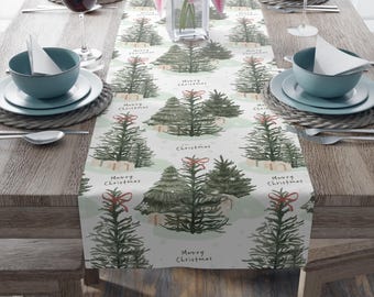 Puede incluir: Un camino de mesa navideño festivo con un patrón repetido de árboles de Navidad en acuarela con lazos rojos y las palabras "Merry Christmas" sobre un fondo claro. El camino de mesa está colocado sobre una mesa de madera con cubiertos.