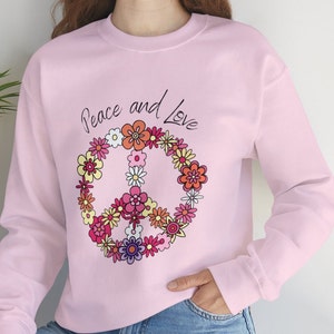 Puede incluir: Sudadera rosa con un símbolo de paz hecho de flores y el texto "Peace and Love" impreso en la parte delantera.