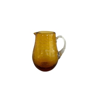 May include: Amber glass pitcher with a clear glass handle. The pitcher has a textured surface and a rounded body.