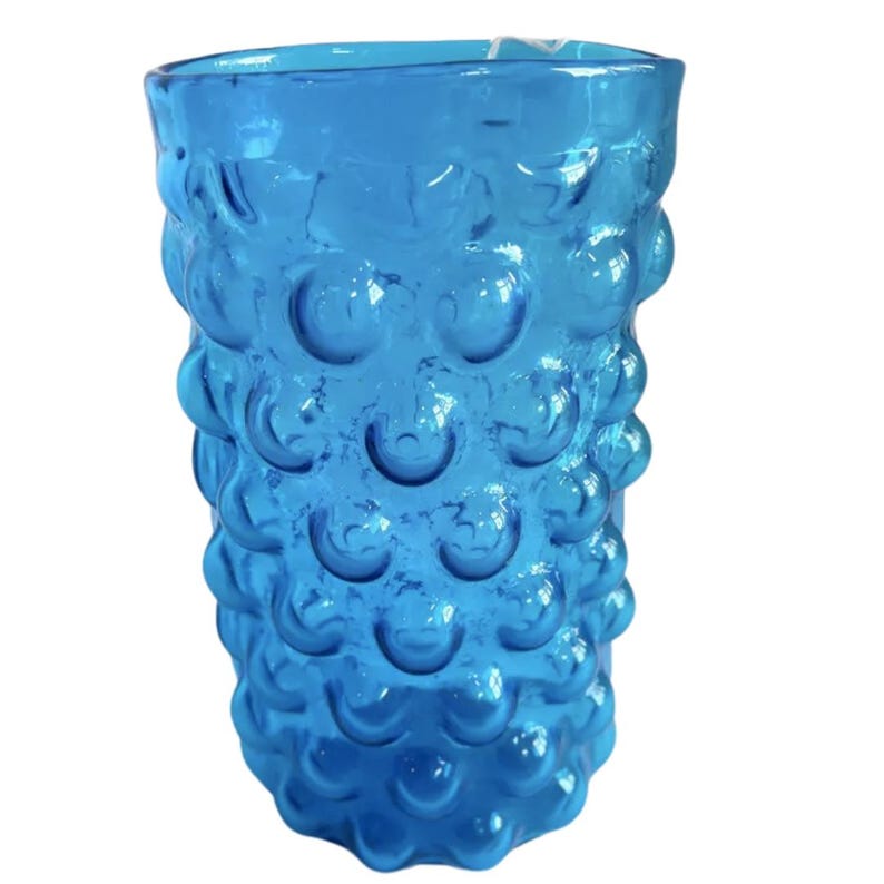 K&ouml;nnte beinhalten: Eine hohe, blaue Glasvase mit einer strukturierten, blasenartigen Oberfl&auml;che. Die Vase ist aus klarem Glas mit einer blauen T&ouml;nung.