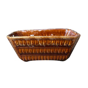 May include: A rectangular ceramic planter with a glossy brown glaze and a textured exterior featuring repeating vertical ridges. The vessel has a wide, open top and a tapered base, showcasing a consistent deep amber color throughout the piece.