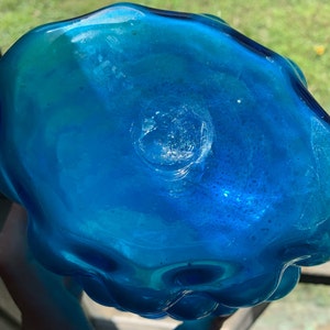 K&ouml;nnte beinhalten: Die Unterseite einer gro&szlig;en, blauen Glasvase mit einer wellenf&ouml;rmigen, organischen Form. Die Vase hat eine kleine, kreisf&ouml;rmige Vertiefung in der Mitte des Bodens.