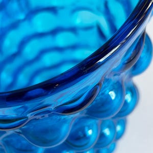 K&ouml;nnte beinhalten: Nahaufnahme einer blauen Glasvase mit einer strukturierten, blasenartigen Oberfl&auml;che.