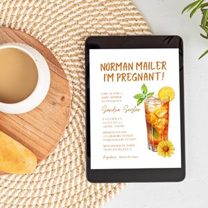 May include: A tablet displays a baby shower invitation with the text "NORMAN MAILER I'M PREGNANT!". The invitation features a watercolor illustration of iced tea with lemon and a sunflower. A cup of coffee and bread sit on a wooden board.