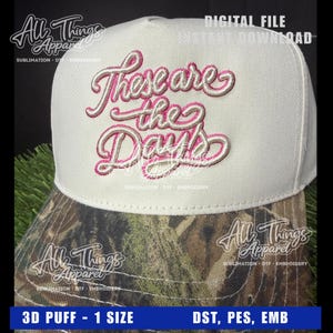 以下が含まれることがあります： 迷彩柄のつばが付いた白い野球帽。「These are the Days」というフレーズがピンクと白の筆記体で刺繍されています。帽子は3Dパフデザインです。