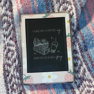 May include: A pink and white patterned case for an e-reader with the text "I like my coffee icy and my books spicy" and a black and white illustration of a stack of books and a boba tea.