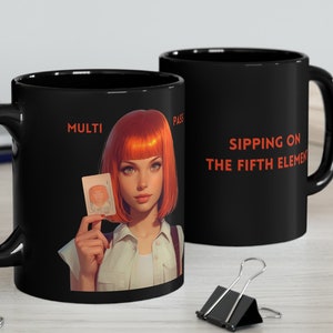 Op de afbeelding: Zwarte koffiemok met een roodharige vrouw die een kaart vasthoudt met de tekst "MULTI PASS" en de tekst "SIPPING ON THE FIFTH ELEMENT".
