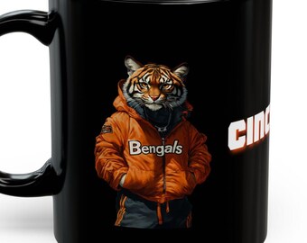 Könnte beinhalten: Schwarze Keramik-Kaffeetasse mit einem Motiv eines Tigers, der eine orange Jacke mit dem Text "Bengals" trägt. Die Tasse hat das Wort "Cincy" an der Seite.