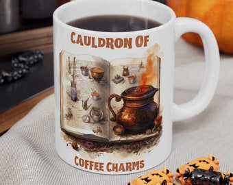 May include: White ceramic mug with a brown and white illustration of a book with a cauldron and the text "Cauldron of Coffee Charms".