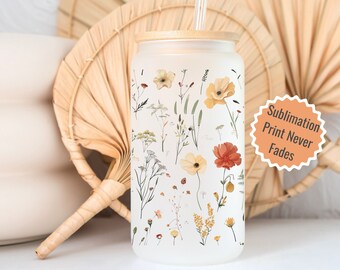 May include: A frosted glass tumbler with a bamboo lid and a clear straw. The tumbler features a floral print with yellow, orange, and red flowers. The text "Sublimation Print Never Fades" is on a sticker.