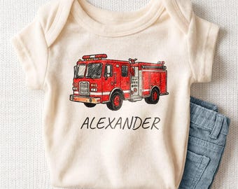 May include: A cream-colored short-sleeve bodysuit featuring a red fire truck illustration with black outlines and the name ALEXANDER printed in black capital letters underneath the vehicle on the front of the garment.