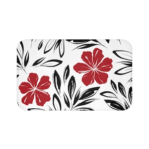 May include: A rectangular bath mat with a white background featuring a repeating pattern of red flowers and black leaves. The flowers have five petals, and the leaves are stylized.