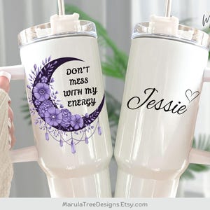 May include: Two white insulated tumblers with handles. One features a purple crescent moon design with flowers and the text "DON'T mess WITH my ENERGY." The other has the name "Jessie" with a heart.