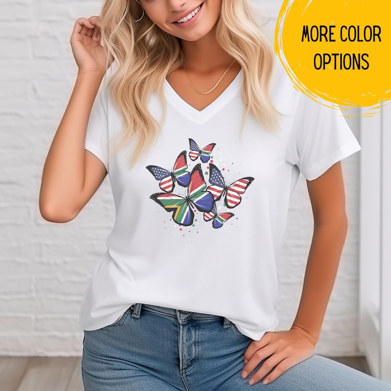 May include: White V-neck t-shirt with a design of butterflies with the American and South African flags on them.  "More Color Options" is written in yellow on a white circle.