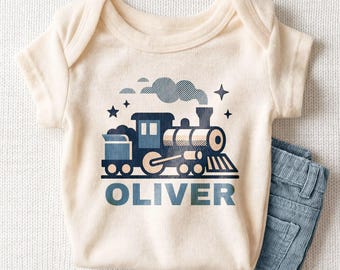 May include: A cream-colored short-sleeve bodysuit featuring a dark blue graphic of a steam locomotive train with smoke, stars, and the name OLIVER printed in bold blue capital letters below the train illustration.