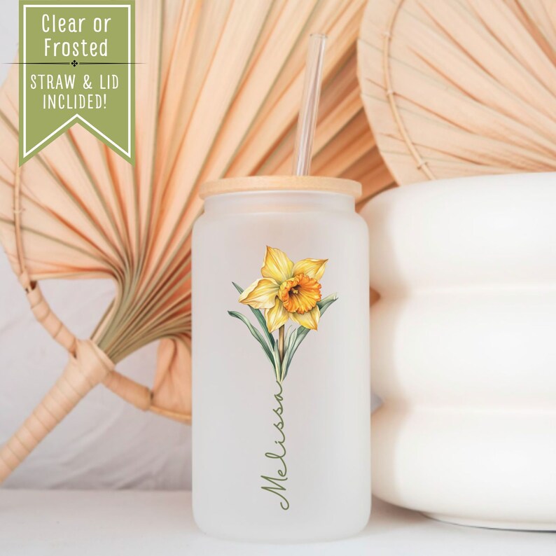 Puede incluir: Un vaso de vidrio esmerilado con tapa de bamb&uacute; y una pajita. El vaso presenta una ilustraci&oacute;n de acuarela de un narciso amarillo y el nombre "Melissa" escrito en cursiva.