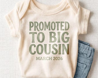May include: A cream-colored short-sleeve baby bodysuit featuring the green text PROMOTED TO BIG COUSIN and MARCH 2026 printed on the front, paired with a pair of blue corduroy pants visible at the bottom right corner of the garment.