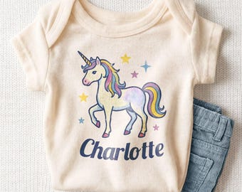 May include: A cream-colored short-sleeve bodysuit featuring a graphic of a unicorn with a multicolored mane and tail, surrounded by small stars. The name Charlotte is printed in dark blue lettering below the unicorn illustration.