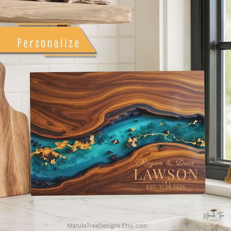 May include: A rectangular wooden cutting board with a river of teal resin and gold leaf accents. The board is personalized with the names "Megan & Dave Lawson" and the date "EST. 11.28.2025". The word "Personalize" is in the upper left corner.