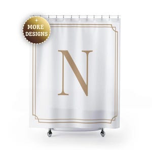 May include: White shower curtain with a large, tan letter "N" in the center, framed by a tan border. The curtain has a gold-colored circular emblem in the upper left corner that says "MORE DESIGNS".