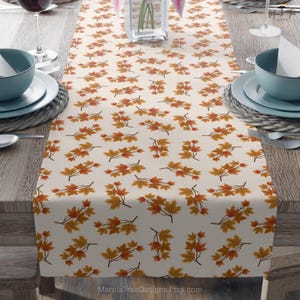 May include: Cream-colored table runner featuring a repeating pattern of autumn maple leaves in shades of orange and yellow. The leaves are arranged on branches, creating a seasonal design. The Etsy shop name, MarulaTreeDesigns.Etsy.com, is visible in the bottom right corner.