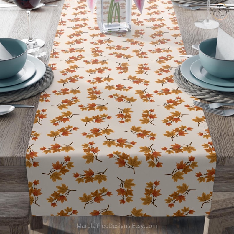 May include: Cream-colored table runner featuring a repeating pattern of autumn maple leaves in shades of orange and yellow. The leaves are arranged on branches, creating a seasonal design. The Etsy shop name, MarulaTreeDesigns.Etsy.com, is visible in the bottom right corner.
