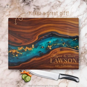 May include: A wooden cutting board with a turquoise river design and gold accents. The board is personalized with the names "Megan & Dave Lawson" and the date "EST. 11.28.2025". A knife and vegetables are next to the board. The text "Makes a great gift!" is also present.