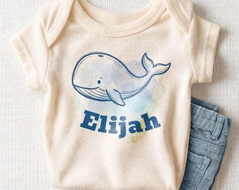 May include: A cream-colored short-sleeve bodysuit featuring a blue line-art illustration of a whale. Below the whale, the name Elijah is printed in bold blue capital letters. The bodysuit is paired with a pair of blue corduroy pants.