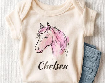 May include: A cream-colored short-sleeve bodysuit featuring a watercolor-style illustration of a pink horse head and the name Chelsea printed in black script lettering below the graphic, paired with blue corduroy pants.