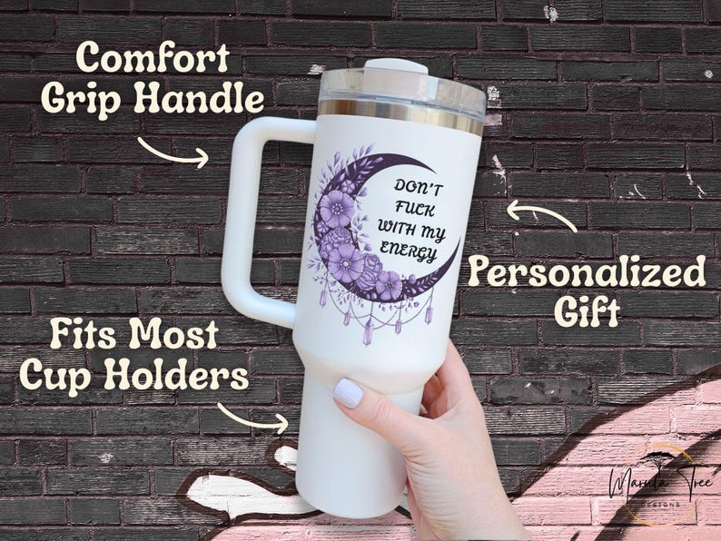 May include: White tumbler with a silver lid and a large white handle. The tumbler features a purple crescent moon design with flowers and the text "DON'T FUCK WITH MY ENERGY". The tumbler is a personalized gift.