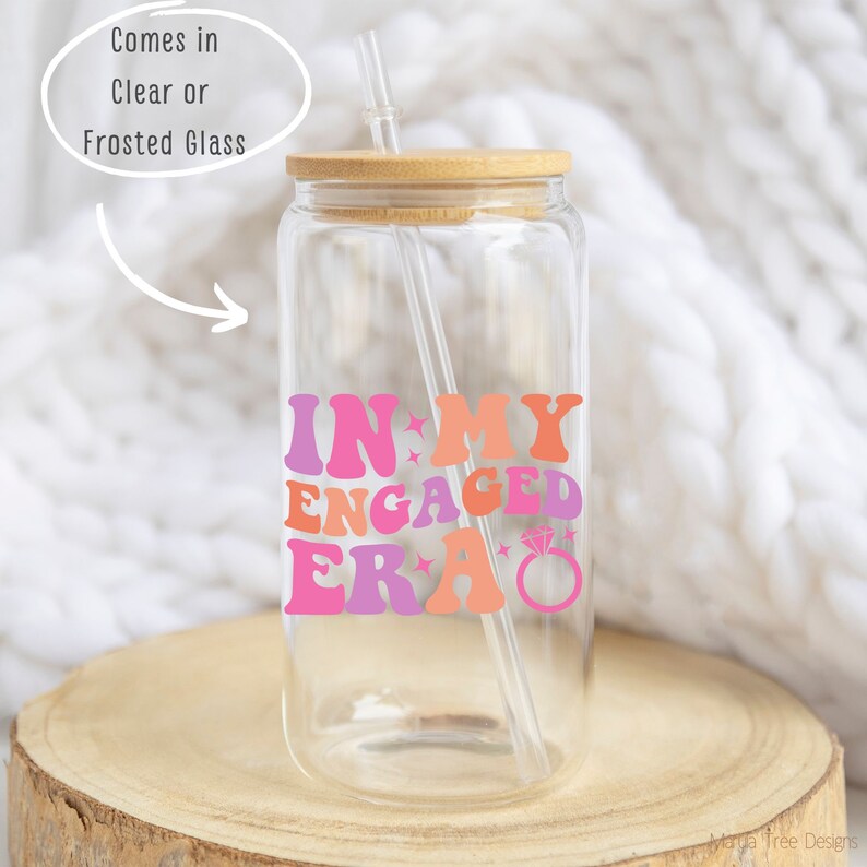 May include: Clear glass tumbler with a bamboo lid and a straw. The tumbler has a pink, orange, and purple graphic that says "In My Engaged Era" with a diamond ring graphic.