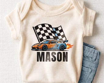 May include: An off-white baby bodysuit featuring a graphic of an orange and blue race car speeding past a checkered flag with flames coming from the rear. The name MASON is printed in large black capital letters below the race car graphic.