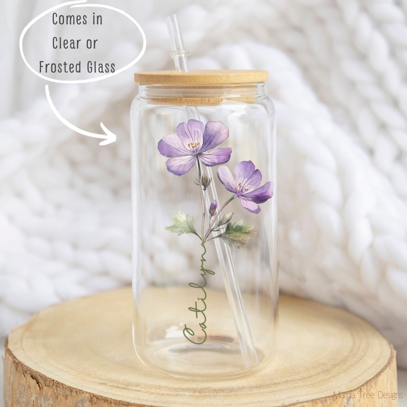 Puede incluir: Un tarro de vidrio transparente con tapa de bamb&uacute; y una pajita. El tarro tiene un dise&ntilde;o de acuarela de flores moradas y el nombre "Caitlyn" escrito en cursiva. El tarro est&aacute; sentado sobre una superficie de madera.