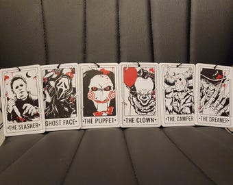 May include: Six rectangular air fresheners featuring horror movie characters. Each card has a black string for hanging and a white border. The characters include The Slasher, Ghost Face, The Puppet, The Clown, The Camper, and The Dreamer.